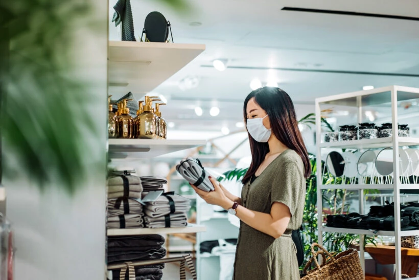 Young asian woman with protective face mask shopping for household necessities in a homeware store looking at a pack of towels